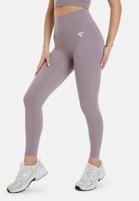Lyse lilla leggings med høj talje, lavet af glat stof, med et hvidt logo på hoften og sømdetaljer langs benene.