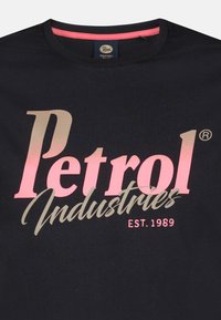 Sort t-shirt med "Petrol Industries" i pink og grå tekst. Runde halsudskæring med en pink detalje. Inkluderet etableret 1989.