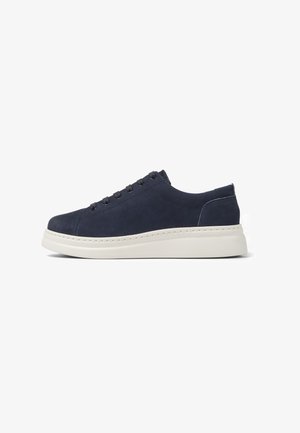 Navy suede sneaker with a rounded toe, five pairs of eyelets, and a white rubber sole. Side stitching detail and soft texture.
