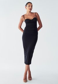 Black satin midi dress with a fitted bodice, adjustable straps, and subtle ruching. Features a front cut-out detail and scalloped hem.