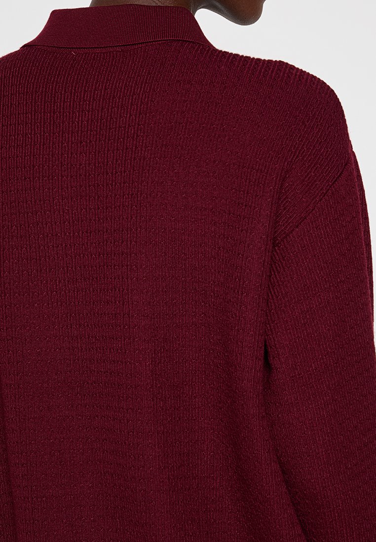 Maglione lavorato a maglia color marrone con una superficie testurizzata, dotato di colletto e design a vestibilità rilassata, che mostra una parte della spalla e della schiena.