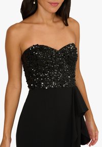 Czarna wieczorowa sukienka z koronkowym bezramiączkowym gorsetem z cekinami, swobodną spódnicą z falbaną oraz dopasowanym fasonem w talii.