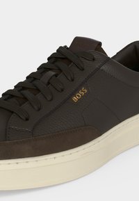Baskets en cuir marron foncé avec lacets noirs, panneaux texturés et en daim, logo doré « BOSS » et semelle en caoutchouc blanche.