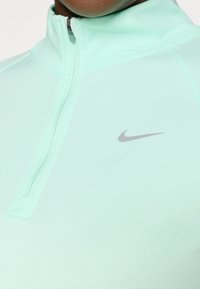 Mintgrønn quarter-zip treningstopp med glatt tekstur, med en liten grå Nike-logo på venstre bryst.