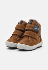 Braune Wildleder-Ankleboots mit weißem Fellfutter, ausgestattet mit zwei Klettverschlüssen und einer Gummisohle, die durch blaue Akzente und Nähte hervorgehoben werden.