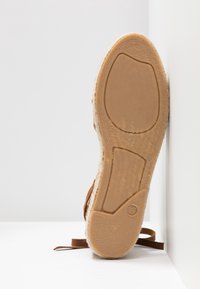 Semelle de sandale en cuir brun avec un fond en caoutchouc texturé, mettant en avant un bord en jute. Taille indiquée comme 37 près du talon.