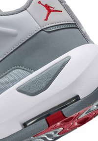 Zbliżenie na piętę szaro-białego buta sportowego z czerwonym logo Jumpman oraz czerwono-szarymi teksturowanymi detalami podeszwy.