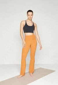 Fekete sportmelltartó és narancssárga, magas derekú leggings, rugalmas anyagból készült, testhezálló kialakítással és sima felülettel, semleges háttér előtt.