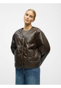 Steppte braune Lederjacke mit großen Fronttaschen, rundem Kragen und Knopfverschluss, kombiniert mit blauen Jeans. Glatte Textur, lockere Passform.