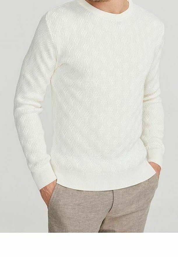 Biały dziergany sweter z fakturowanym wzorem, okrągłym dekoltem i ściągaczami na rękawach, w połączeniu z jasnobeżowymi spodniami.