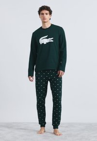 Parte superior de pijama de manga larga verde oscuro con gráfico de cocodrilo blanco, combinada con pantalones verde oscuro con pequeños patrones de nubes blancas.