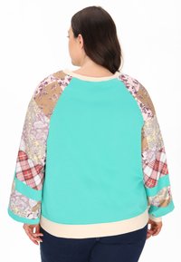 Felpa over-size color teal con maniche a motivi multicolori che presentano design paisley, floreali e a quadri; colletto e polsini a costine.