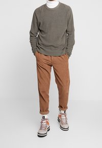 Helles olivfarbenes geripptes Sweatshirt, tanfarbene Corduroyhose und mehrfarbige Schnürstiefel mit weißen Akzenten und schwarzem Absatz.