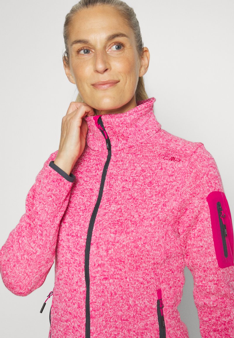 Giacca in pile di un vivace color rosa con colletto alto, zip nera e tasche. Presenta un tessuto testurizzato e una toppa a contrasto sulle spalle.