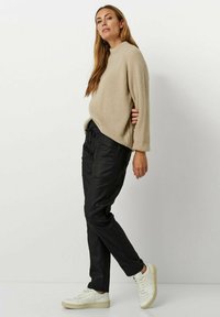 Beige gestrickter Pullover mit Rundhalsausschnitt, kombiniert mit schwarzen schmal geschnittenen Hosen. Weiße minimalistische Sneaker runden das lässige Outfit ab.