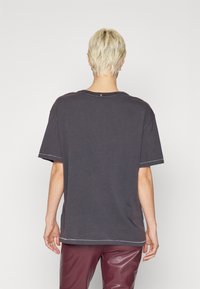 Kortärmad, oversized t-shirt i mörkgrå bomull, med synliga sömsynpunkter och en avslappnad passform, sedd bakifrån.