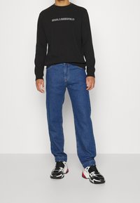 Felpa nera a maniche lunghe con logo "KARL LAGERFELD", abbinata a jeans blu a gamba dritta e sneakers bianche e nere.