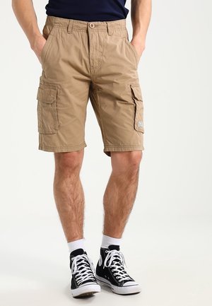 Beiget, kevyestä kankaasta valmistetut cargo-shortsit, joissa useita sivutaskuja, löysä istuvuus ja suora leikkaus. Käytetty mustien tennareiden kanssa.