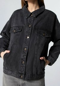 Giubbotto di jeans nero con chiusura a bottone, due tasche sul petto e colletto. Presenta una vestibilità comoda e dettagli di cucitura a vista.