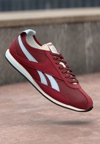 Ténis vermelhos com detalhes em azul claro, parte superior em couro, bico redondo, atacadores à frente e sola em borracha branca. Apresenta um design vintage.