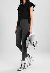 Blusa negra con volantes, vaqueros pitillo grises y botines plateados con punta afilada. Accesorio: mochila metálica plateada con cierre de solapa.