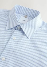 Camisa de rayas azul claro con cuello abotonado, con botones blancos, tela nítida y una etiqueta que dice "NEXT" en el interior del cuello.