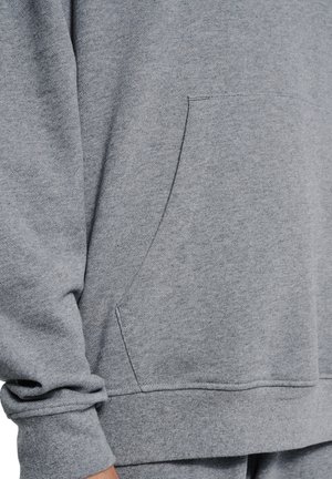 Close-up van een persoon die een grijze trui draagt met een voorzak en bijpassende joggingbroek.