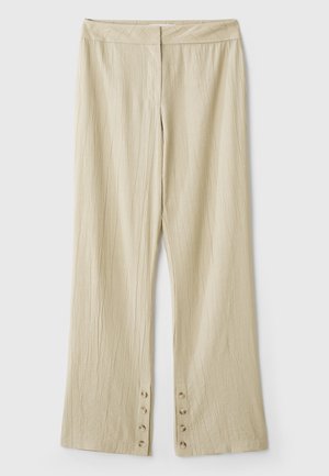Pantaloni larghi beige realizzati in tessuto testurizzato. Presentano una vita piatta e cinque bottoni all'orlo per la chiusura. Design con pieghe.