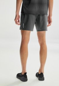 Grå sportsshorts med en glat overflade, der har et lille hvidt logo-detalje. Sorte letvægts-sko med en struktureret sål og en løkke.