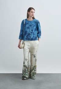 Τζιν τοπ με κεντήματα από λουλούδια σε μπλε χρώμα, συνδυασμένο με εκρού παντελόνι φαρδιάς γραμμής με πολύχρωμο βοτανικό σχέδιο. Τσάντα με λουράκι αλυσίδα και κοσμήματα.