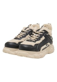 Chunky sneakers met beige fleece voering, zwarte leren panelen, beige veters en dikke beige rubberen zolen tegen een witte achtergrond.