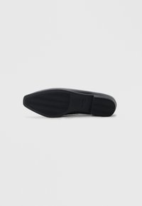 Chaussure noire en cuir avec une tige en cuir lisse et une semelle en caoutchouc texturée. Présente un bout arrondi et un design épuré et minimal.