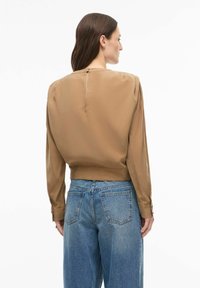 Blouse en soie marron avec manches longues, taille cintrée et fermeture à boutons dans le dos, associée à un jean en denim bleu taille haute.