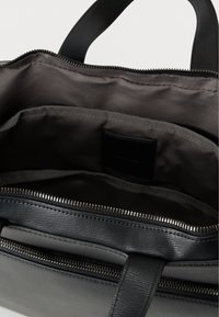 Μαύρη δερμάτινη τσάντα με απαλή υφή, κλείσιμο με φερμουάρ και διπλές χειρολαβές. Εσωτερικά διαθέτει γκρι υφασμάτινη επένδυση και πολλαπλά διαμερίσματα για οργάνωση.