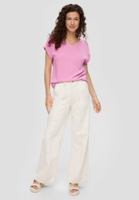 Roze kortmouw v-hals top gecombineerd met wijde crèmekleurige broeken met zichtbare stiksels, aangevuld met lichtgekleurde platform sandalen.