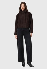 Giacca corta marrone scuro in finta pelle scamosciata con collo alto, abbinata a jeans neri a gamba larga e stivaletti neri con punta affilata.