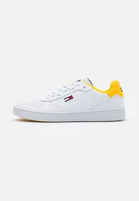White leather sneaker with yellow accents on heel. Features lace-up closure, rubber sole, and a logo on the side. Clean design, minimal details.