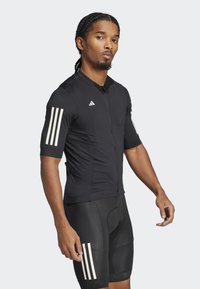 Black cycling jersey with short sleeves, front zipper, and three white vertical stripes on each sleeve. Worn with black cycling shorts.