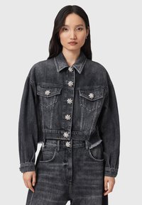 Chaqueta recortada de mezclilla negra con mangas oversized, cinco adornos en forma de flor, dos bolsillos en el pecho y detalle de dobladillo deshilachado.