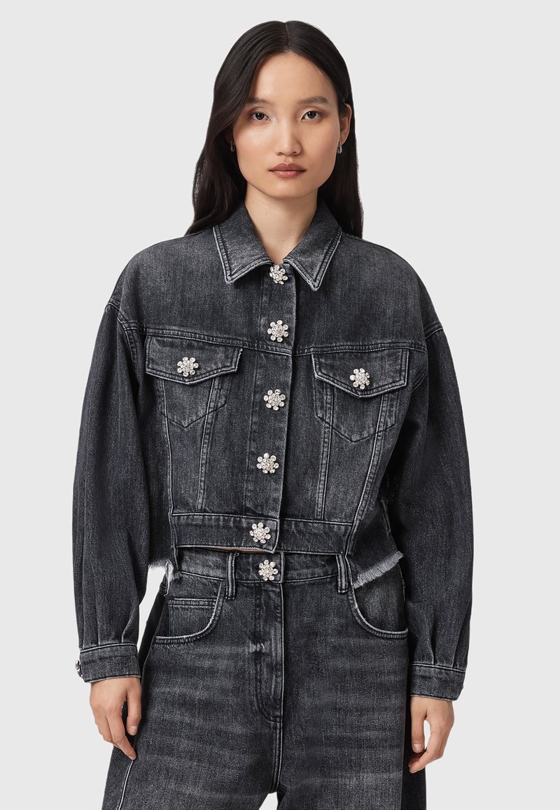 Chaqueta recortada de mezclilla negra con mangas oversized, cinco adornos en forma de flor, dos bolsillos en el pecho y detalle de dobladillo deshilachado.