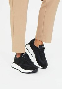Zapatillas negras con una mezcla de texturas suaves y de ante, suela blanca, diseño moderno y marcas en la lengüeta y el panel lateral.