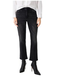 Jeans neri in denim con taglio dritto, cinque tasche e una texture leggermente sbiadita, abbinati a stivaletti neri a punta con tacco a stiletto.