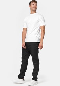Hvid t-shirt med korte ærmer, sorte jeans og hvide sneakers. T-shirten er ensfarvet; jeansene har en standard pasform og minimale syninger.