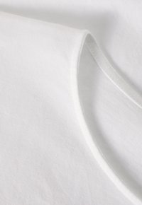 Tessuto di cotone bianco con una texture morbida, caratterizzato da un collo tondo e cuciture lisce e pulite lungo il bordo.