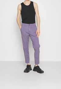 Fialové úzké kalhoty z tkaniny twill, s předními kapsami a zapínáním na knoflík, v kombinaci s černým topem bez rukávů a černými teniskami.