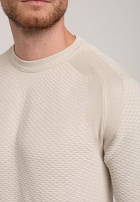 Hellbeiger Strickpullover mit einem strukturierten Rautenmuster, rundem Hals und gerippten Bündchen. Das Design weist eine leicht taillierte Passform auf.
