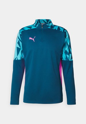 Half-zip lange mouw pullover in donker teal met geometrische turquoise mouwen en roze accenten; beschikt over een textuurstof en een Puma-logo.