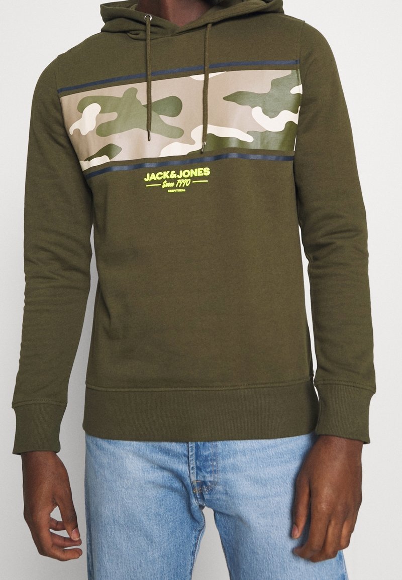 Sudadera verde hecha de una mezcla de algodón, con un patrón de camuflaje en el pecho, detalles en azul y un logo en amarillo brillante.