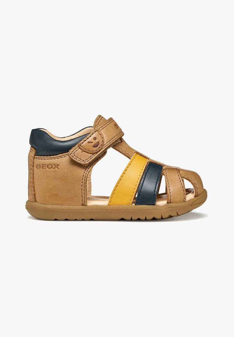 Sandale pour tout-petit en cuir tan avec des brides bleu marine et jaune, fermeture Velcro à la cheville, bout arrondi et semelle marquée pour une utilisation en extérieur.