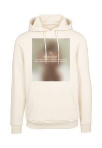 Cremefarvet hoodie med en frontlomme, snørelukning i hætten og et kvadratisk grafisk motiv, der viser en sløret besked om følsomt indhold.